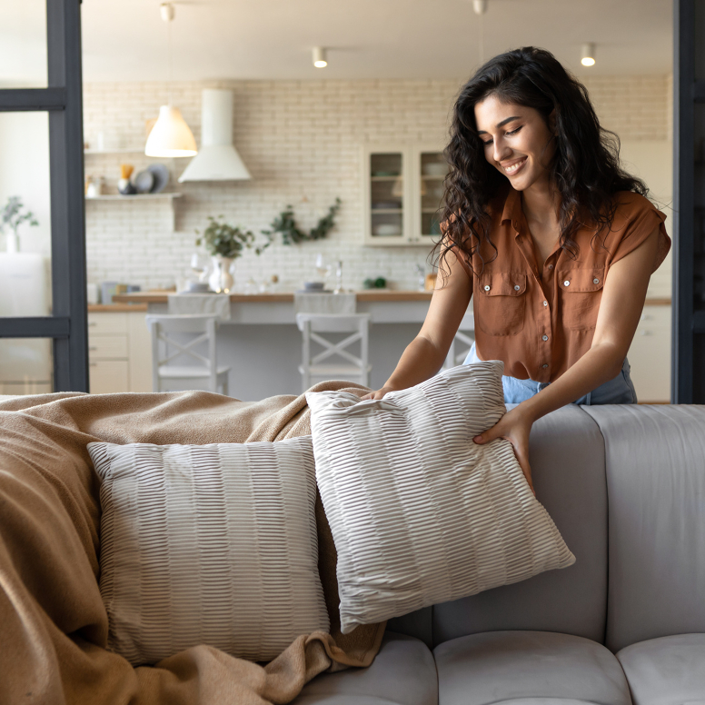 Lächelnde Frau richtet Dekokissen auf einem Sofa.