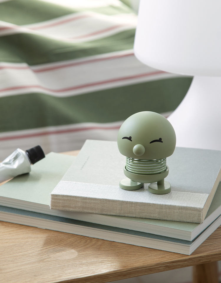 Pastellgrüner Hoptimist steht auf Büchern auf einem Nachttisch.